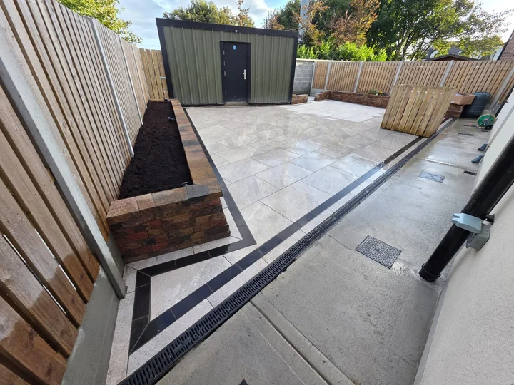 Dark paving border, raised bed and drainage channel beside the porcelain patio.