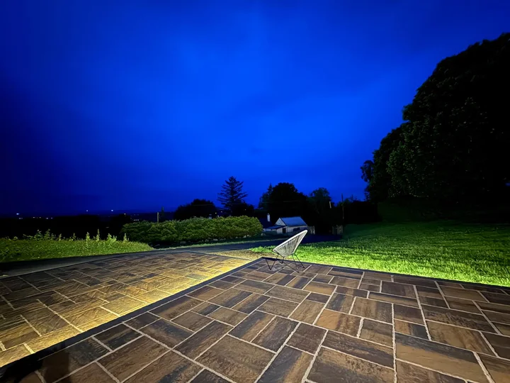 The stone-house patio at dusk, looking across the paving towards the lawn