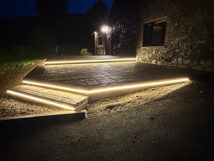 An evening view of the paved terrace and illuminated steps beside the stone house
